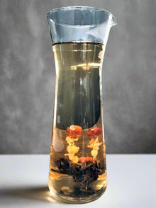 Glass carafe with tea leaves and flowers on a gray background