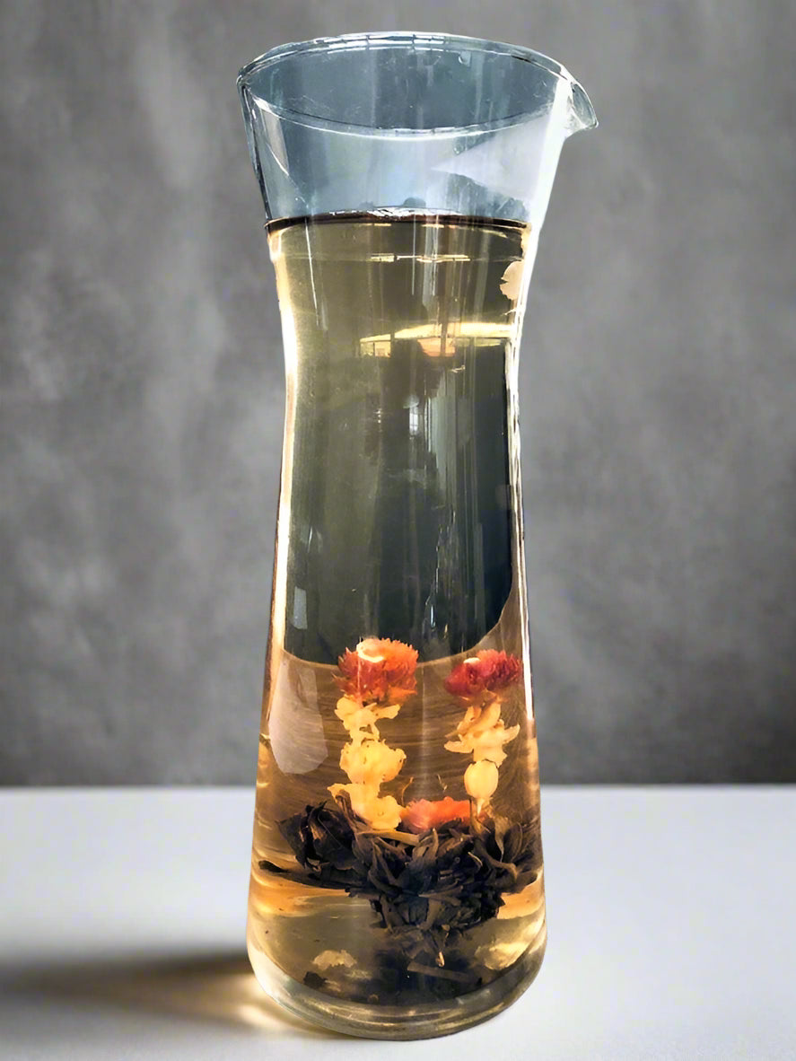 Glass carafe with tea leaves and flowers on a gray background