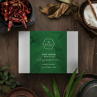 A box of Nasi Lemak tea blend surrounded by dried pandan leaves, dried chilli, and other tea making ingredients, presented on a wooden surface.